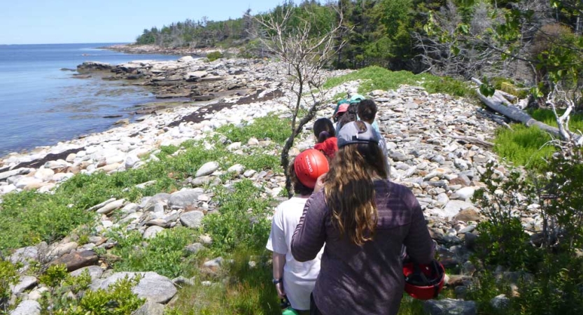 A group of students hike along a rocky shoreline 